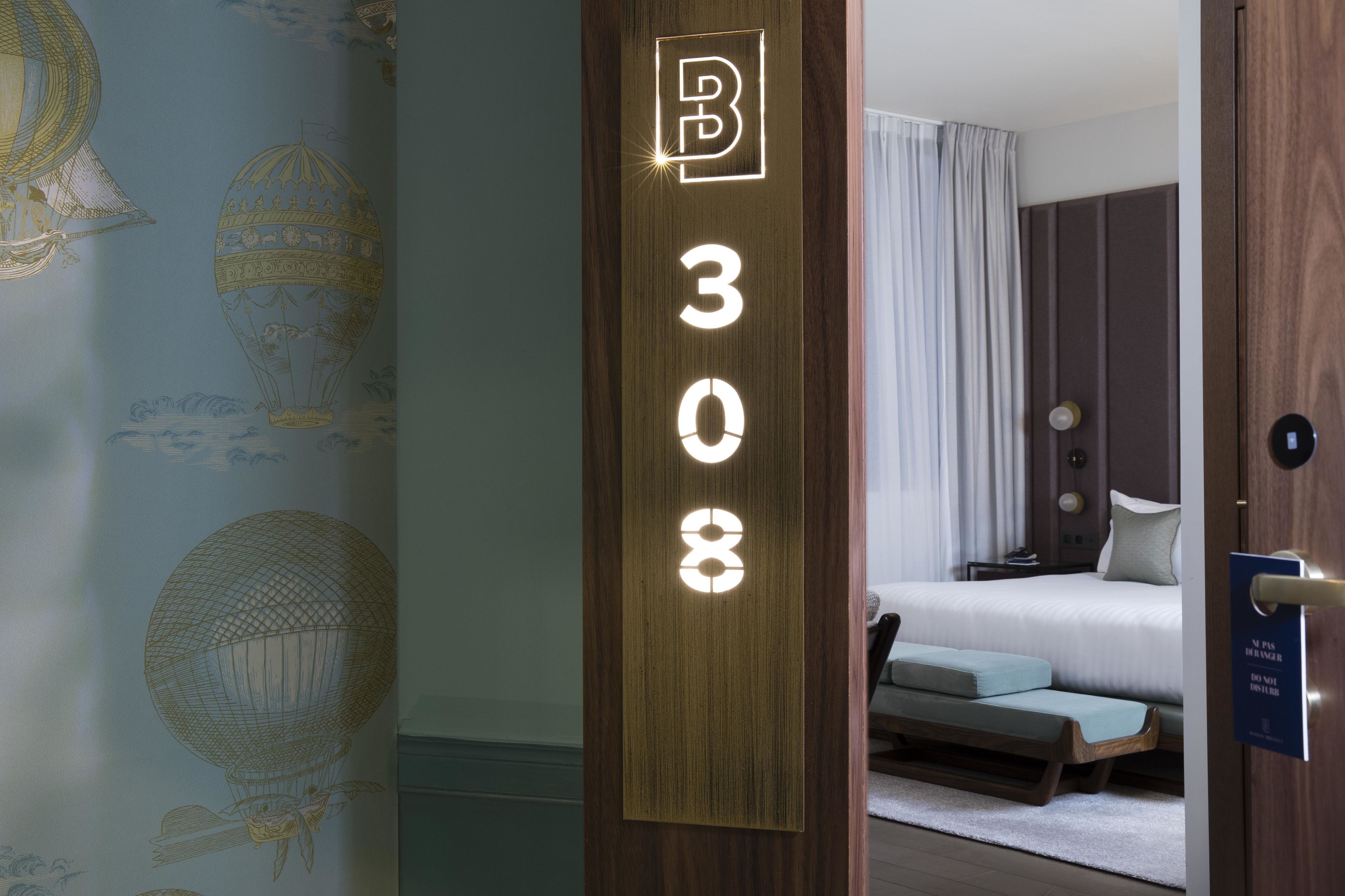 A hotel room with a bed, a bench, and a door with a sign.