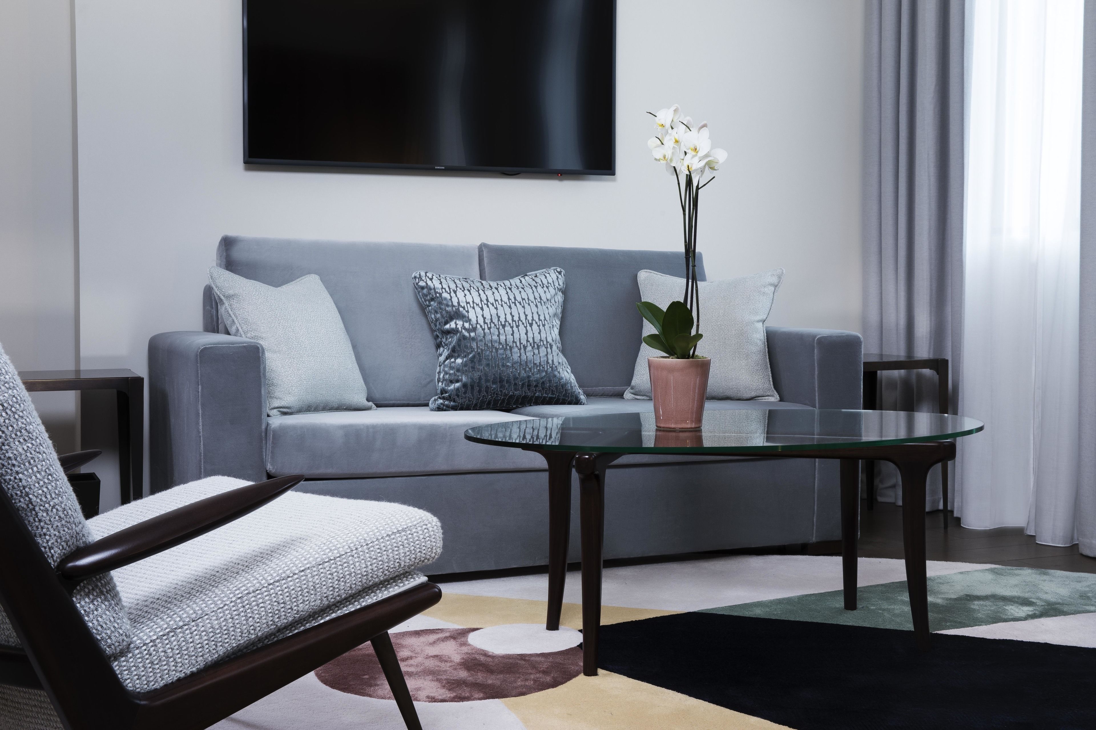 A modern living room with a grey sofa, a glass coffee table, and a potted orchid.