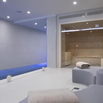 A modern spa room with a large bathtub, seating area, and a wooden wall with a clock.