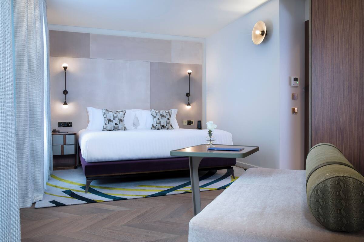 A modern hotel room with a large bed, bedside tables, a small desk, and a sofa.