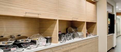 A modern kitchen with wooden cabinets, stainless steel appliances, and a long counter.