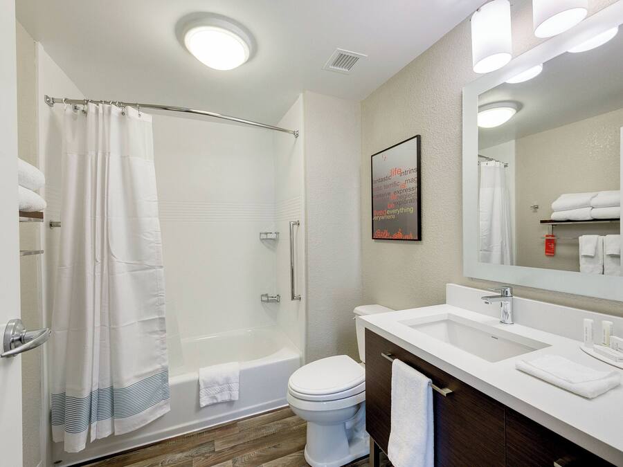A modern bathroom with a shower, toilet, and sink, featuring a mirror, towel rack, and a framed artwork on the wall.