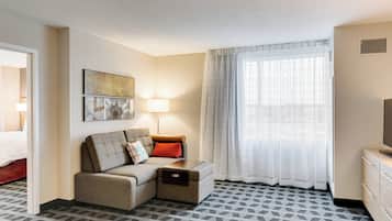 A hotel room with a sofa, a small table, a lamp, a TV, and a window with curtains.