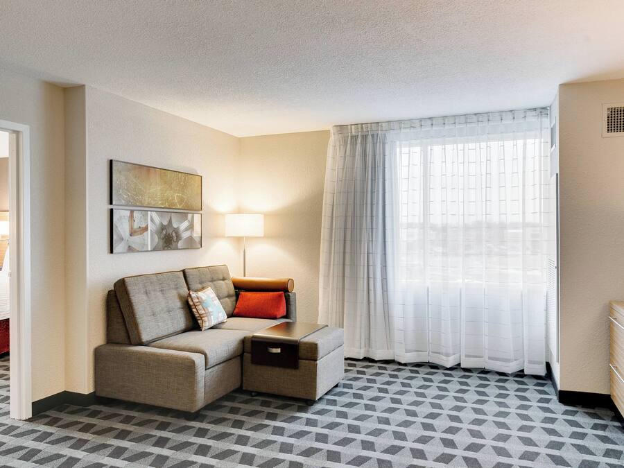 A hotel room with a sofa, a small table, a lamp, a TV, and a window with curtains.