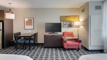 Habitación de hotel con una cama, un escritorio con silla, televisor, una mesita de noche con lámpara y un sillón rojo.