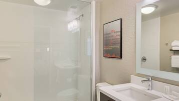 A modern bathroom with a glass-enclosed shower, a large mirror, and a white sink.
