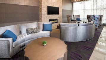 A modern living room with a stone accent wall, a flat-screen TV, a fireplace, and a large round coffee table.