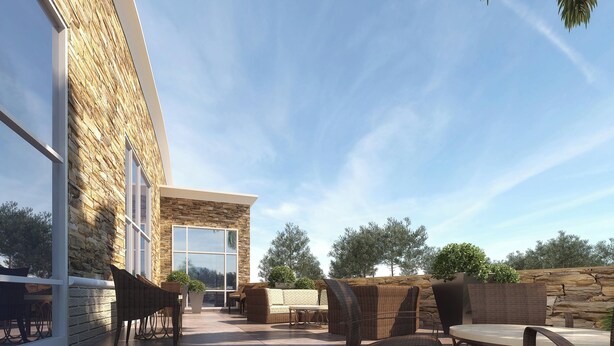 An outdoor patio with wicker furniture, a stone wall, and a large window.