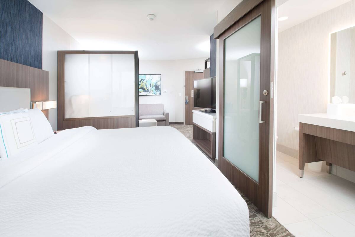 A hotel room with a large bed, a desk, a television, and a bathroom with a mirror and sink.