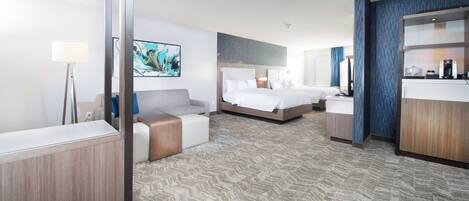 A hotel room with a large bed, a sofa, a desk, and a kitchenette.