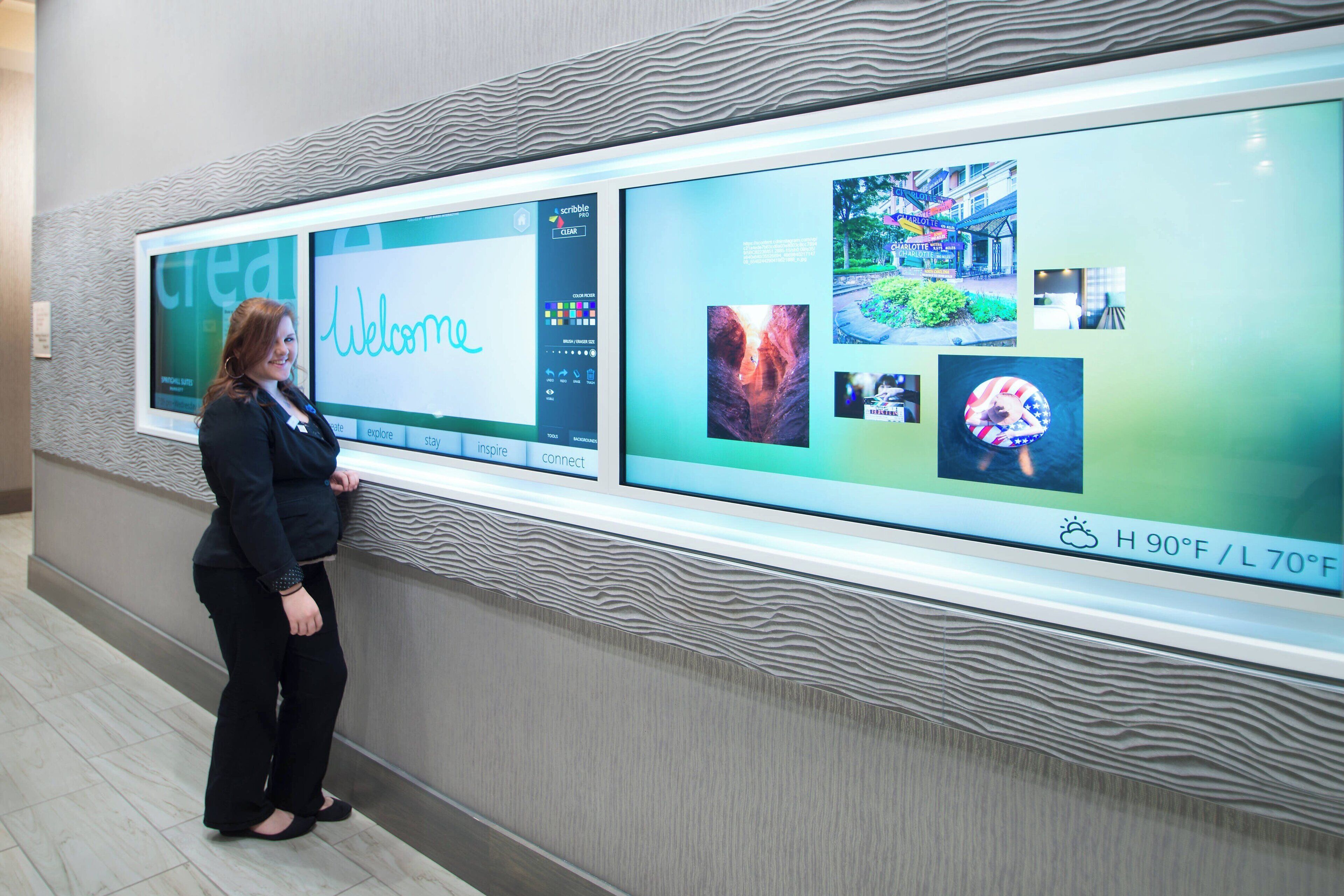 A woman standing in front of a digital display with a 'Welcome' message and various images.