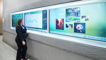 A woman standing in front of a digital display with a 'Welcome' message and various images.