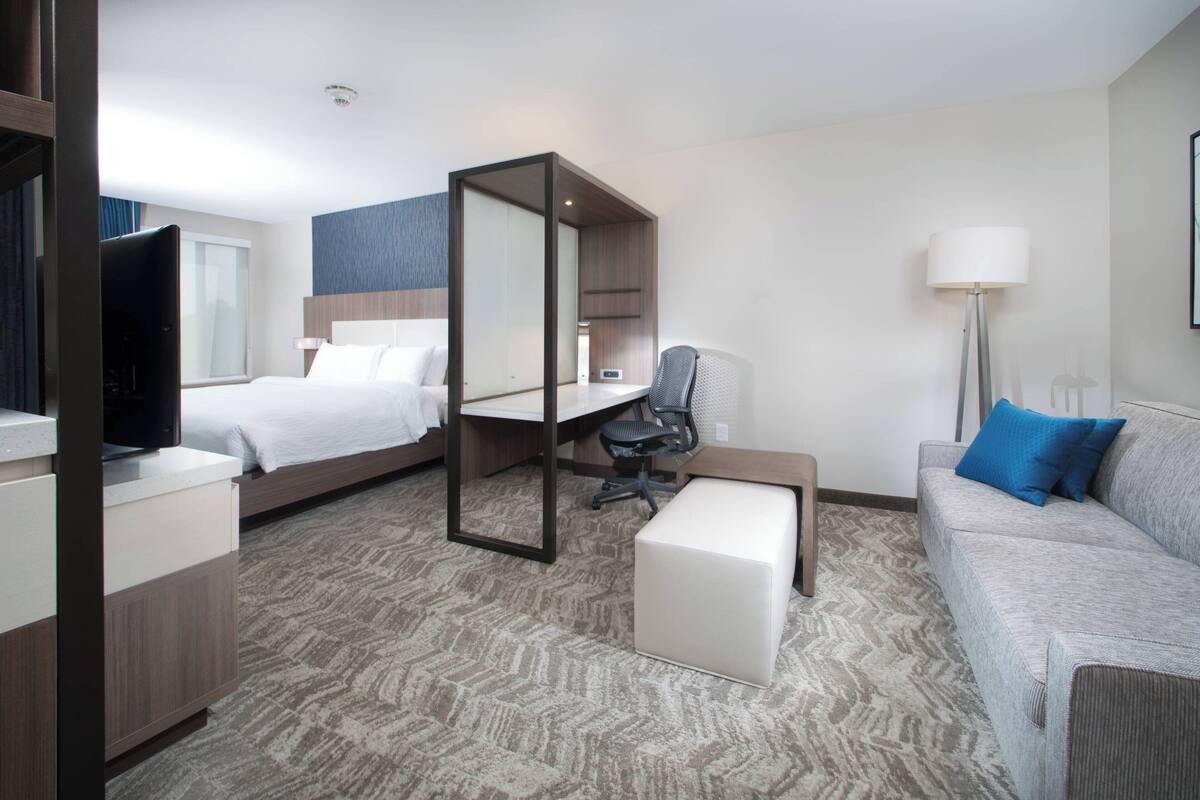 A hotel room with a bed, a desk, a chair, a sofa, and a TV.