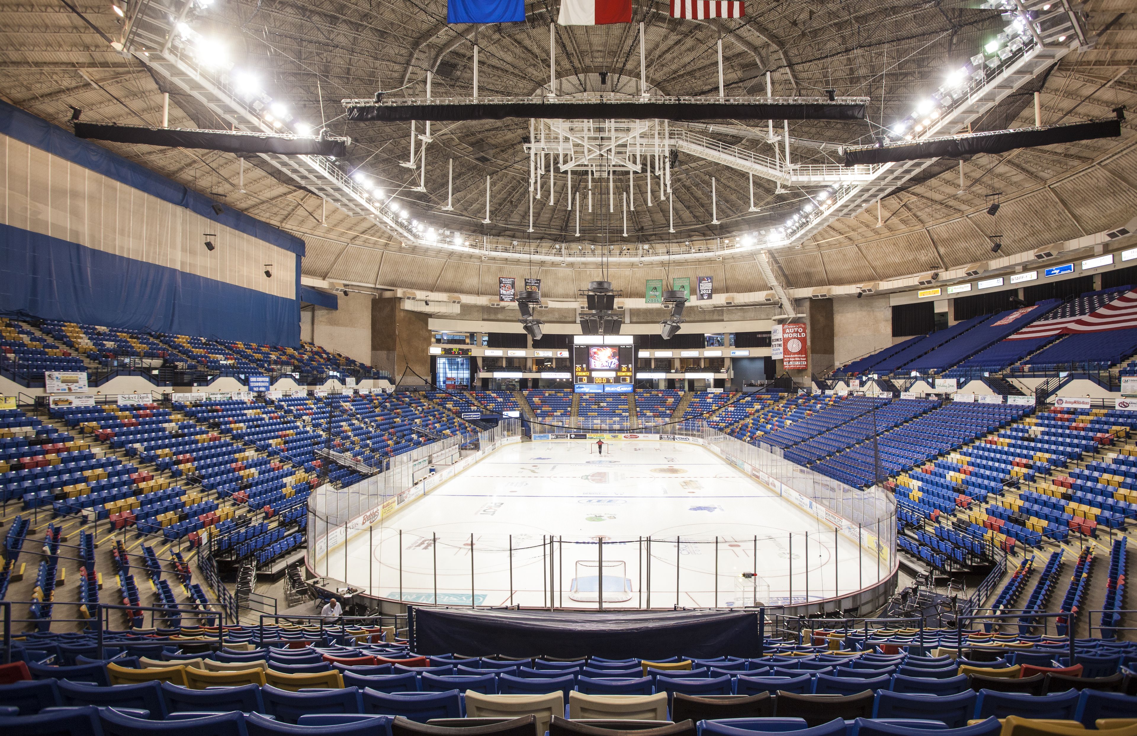 An indoor sports arena with multiple seating sections, a central ice rink, and overhead lighting.