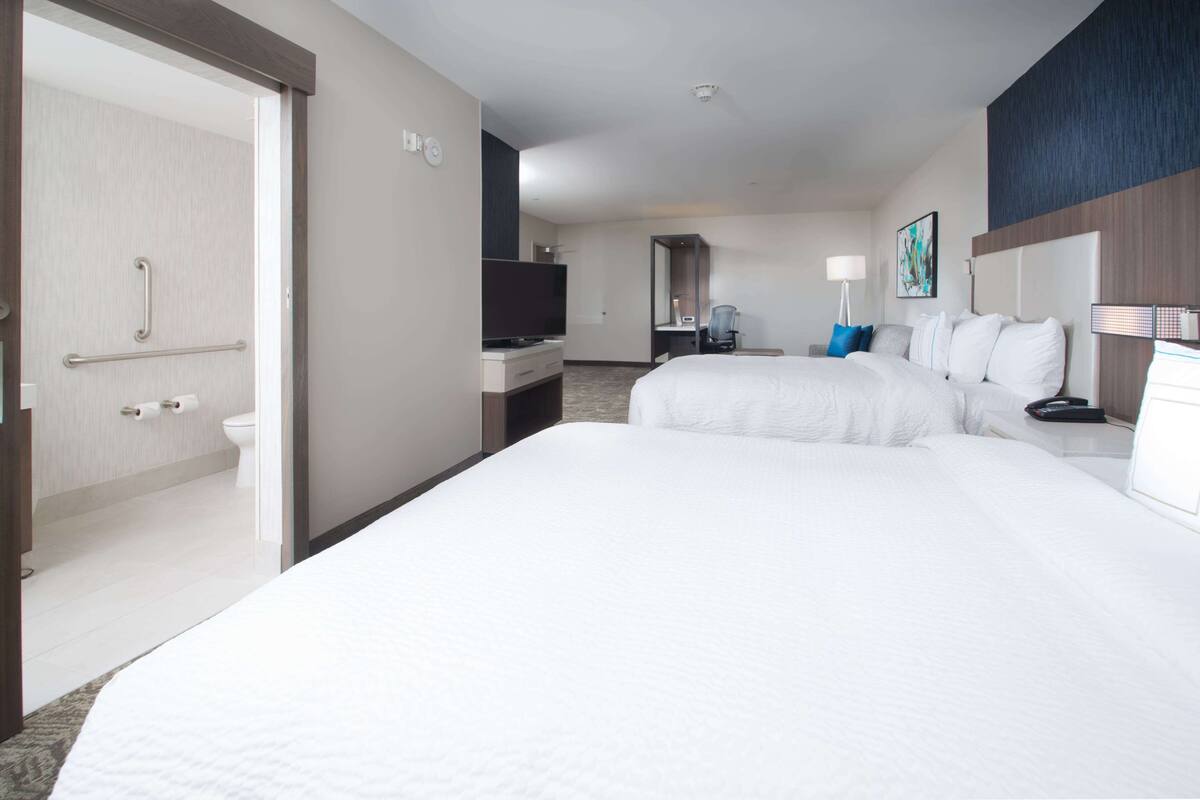 A hotel room with a large bed, a desk with a computer, a TV, and a bathroom with a toilet and shower.