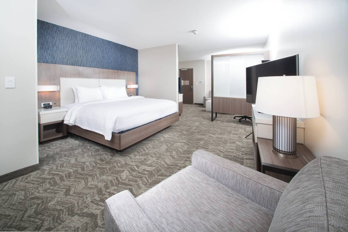 A hotel room with a large bed, a desk with a lamp, a television, and a sofa.