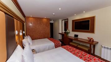 A hotel room with two beds, a desk, a mirror, and a television.