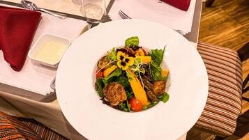 Una mesa de comedor con un plato blanco de ensalada, un cuenco pequeño para el aderezo y un vaso de agua.