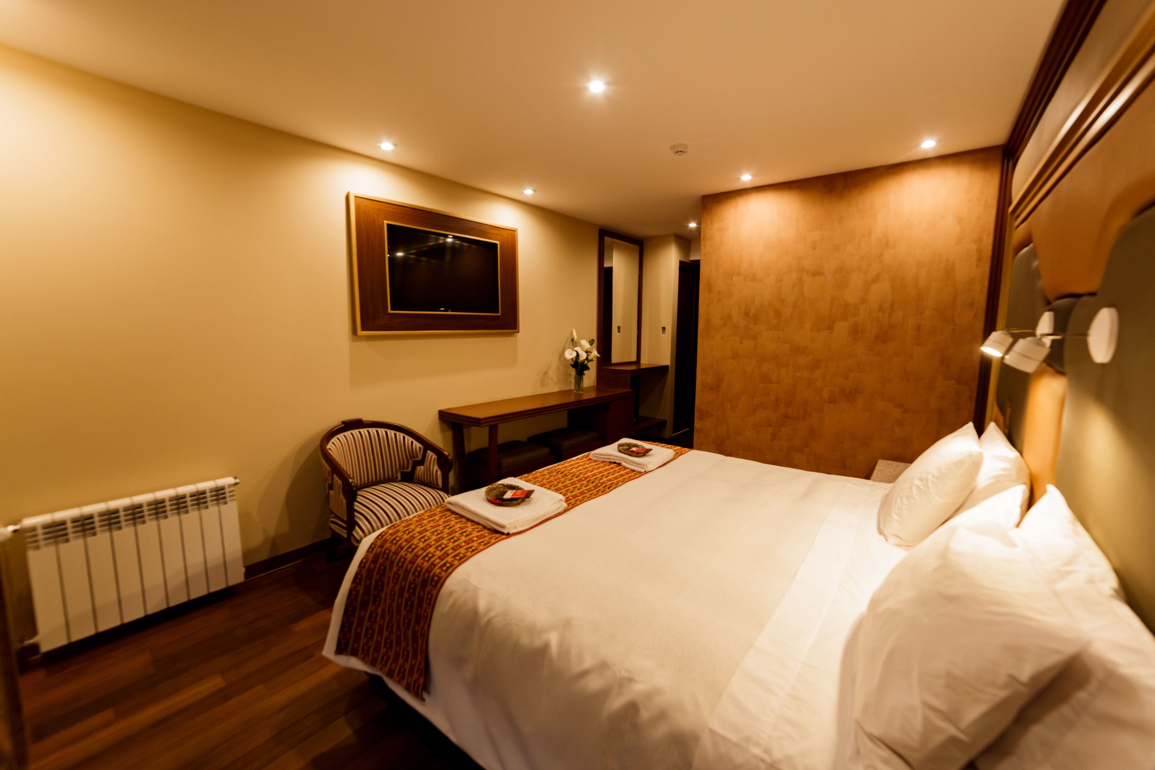 A hotel room with a large bed, a wooden desk, a chair, and a radiator.