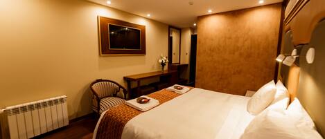 A hotel room with a large bed, a wooden desk, a chair, and a radiator.