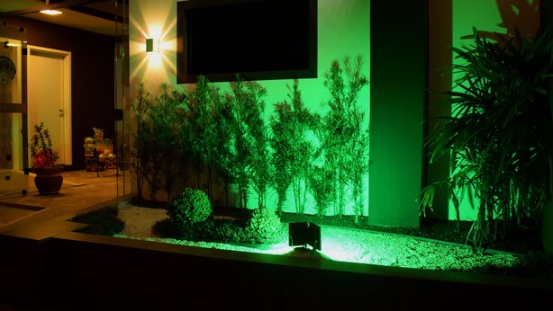 A modern building with a green-lit vertical garden, a flat-screen TV mounted on the wall, and a potted plant on the right. - Hotel Pousada Estrela do Mar (Penha)
