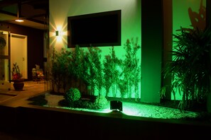 Un edificio moderno con jardín vertical iluminado en verde, un televisor de pantalla plana en la pared y una planta en maceta a la derecha.