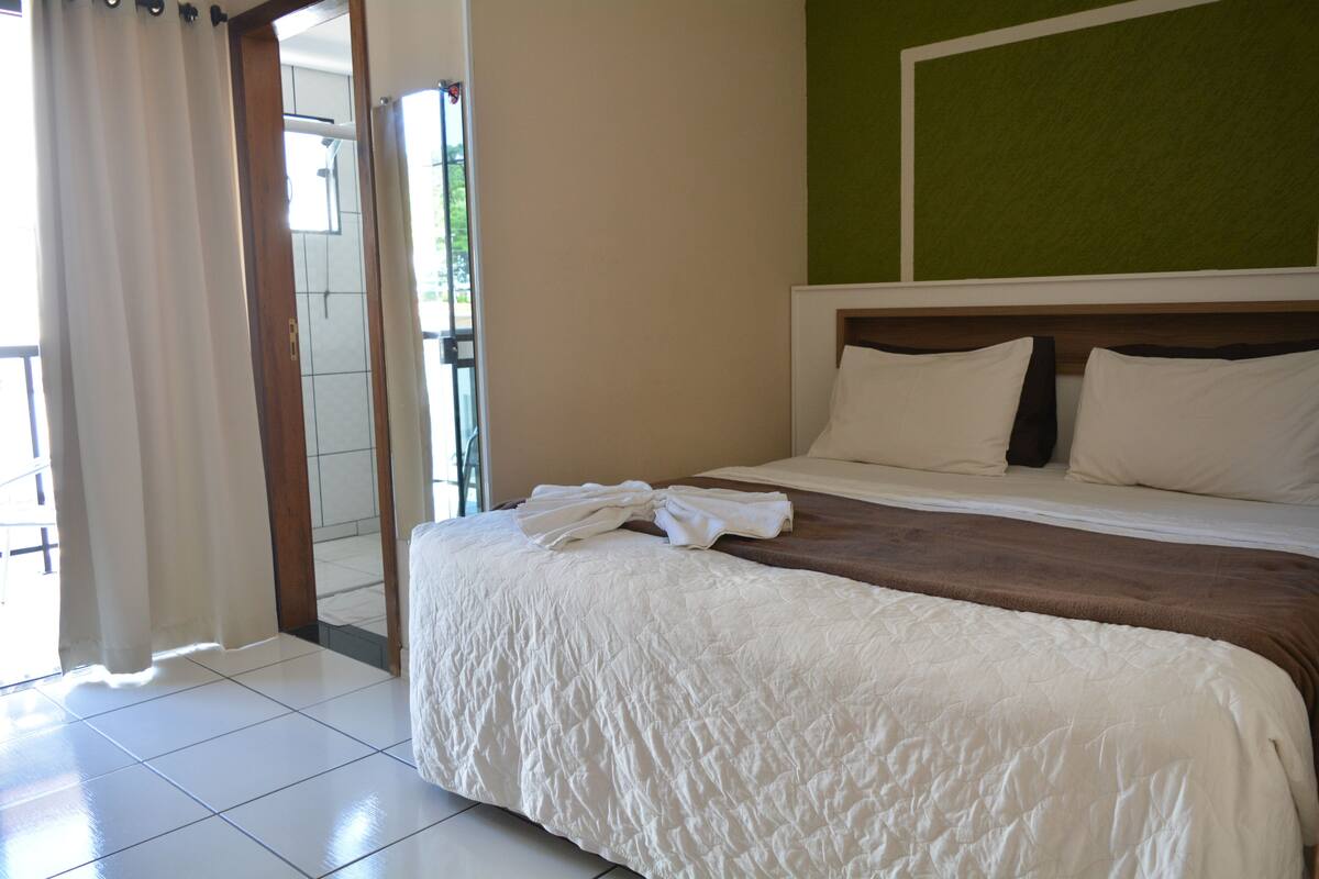 A hotel room with a bed, a green wall, and a view through an open door.