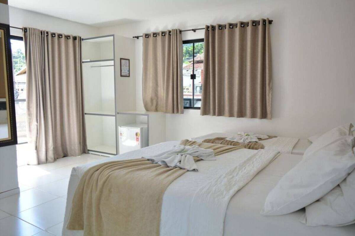 A hotel room with a bed, curtains, a window, and a door.