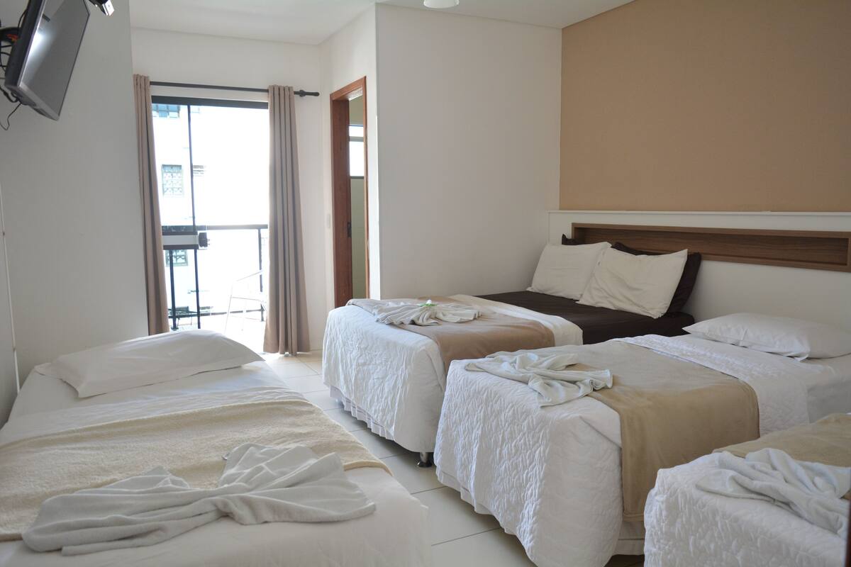 A hotel room with three beds, a TV, and a balcony with curtains.