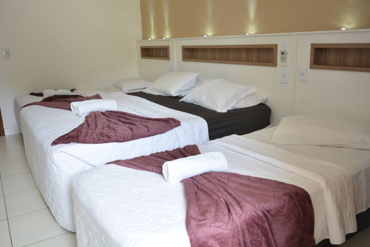 A hotel room with three beds, each with white bedding and a brown blanket.