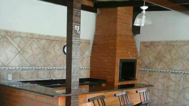 A kitchen area with a brick counter, a built-in oven, and a bar stool seating arrangement. - Hospedagem Victorino (Penha)