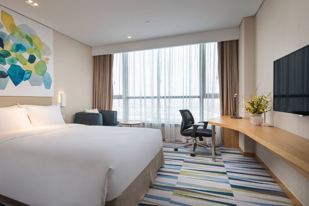 A hotel room with a large bed, a desk, a chair, a TV, and a window with curtains.