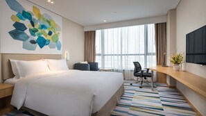 A hotel room with a large bed, a desk, a chair, a TV, and a window with curtains.