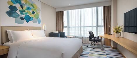 A hotel room with a large bed, a desk, a chair, a TV, and a window with curtains.