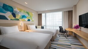 A hotel room with two beds, a desk, a chair, a TV, and a large abstract painting on the wall.