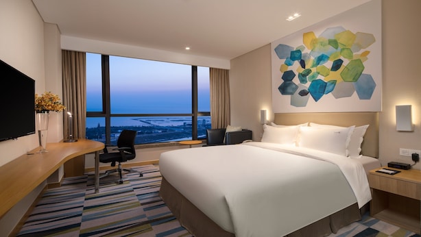 A hotel room with a large bed, a desk with a chair, a TV, and a view of the cityscape through large windows. - Holiday Inn Express Suzhou Taihu Lake by IHG (Suzhou)