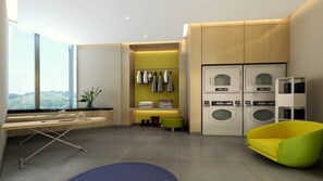 A modern laundry room with built-in washers and dryers, a seating area with a yellow chair, and a view of greenery outside. - Holiday Inn Express Suzhou Taihu Lake by IHG (Suzhou)