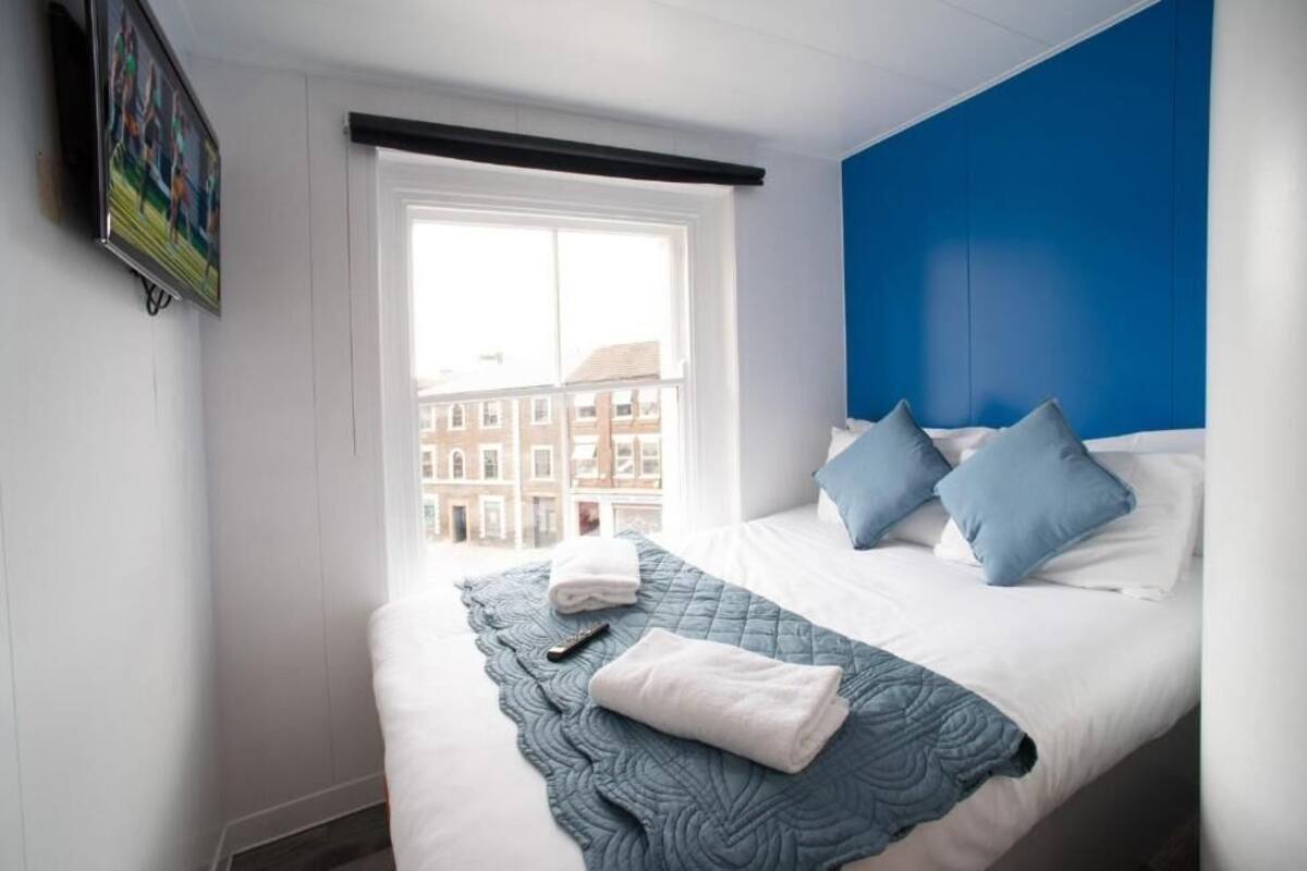 A hotel room with a bed, a window with a view of buildings, and a blue accent wall.