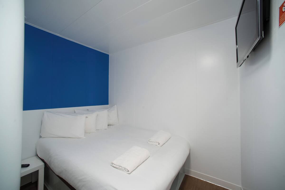 A hotel room with a bed, white bedding, a blue accent wall, and a mounted TV.