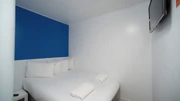 A hotel room with a bed, white bedding, a blue accent wall, and a mounted TV.