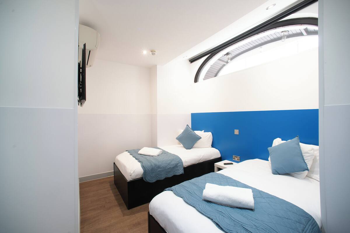 A modern hotel room with two beds, a skylight, and a small bedside table.