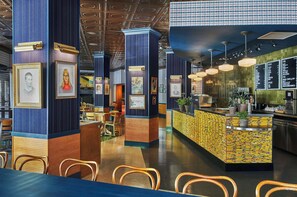 A restaurant interior with high ceilings, framed portraits on columns, a counter with a yellow patterned backsplash, and a menu board.