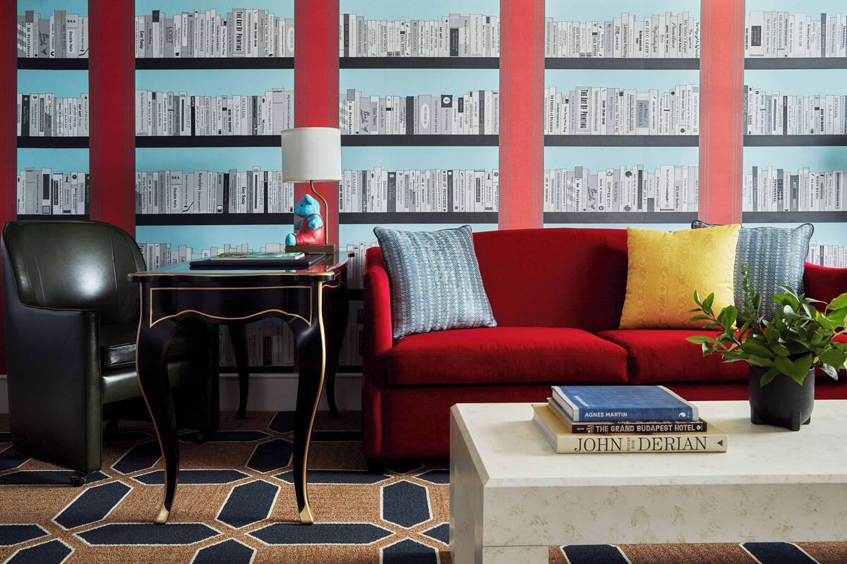Ein modernes Wohnzimmer mit einem roten Sofa, einem gemusterten Teppich und einem Bücherregal voller Bücher.