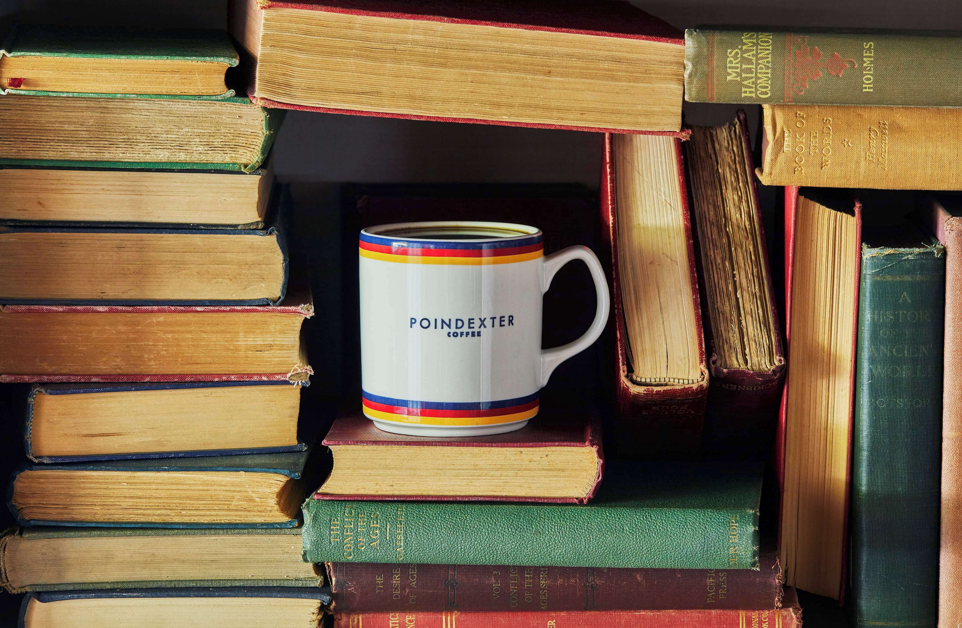 A stack of books with a mug labeled "POINDEXTER COFFEE" on top.