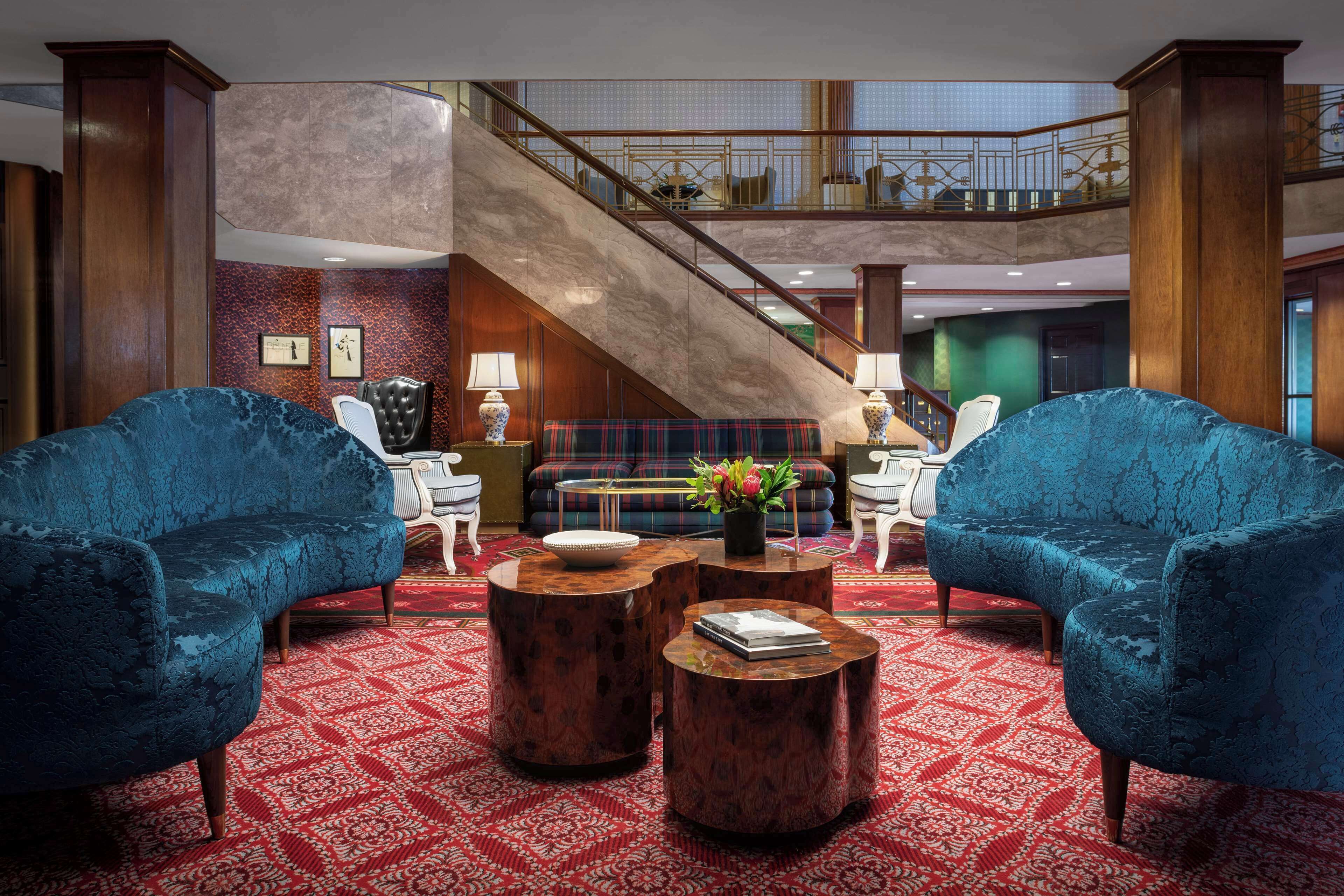 A lobby with two blue armchairs, a red patterned carpet, a staircase, and a seating area with a sofa and coffee table.