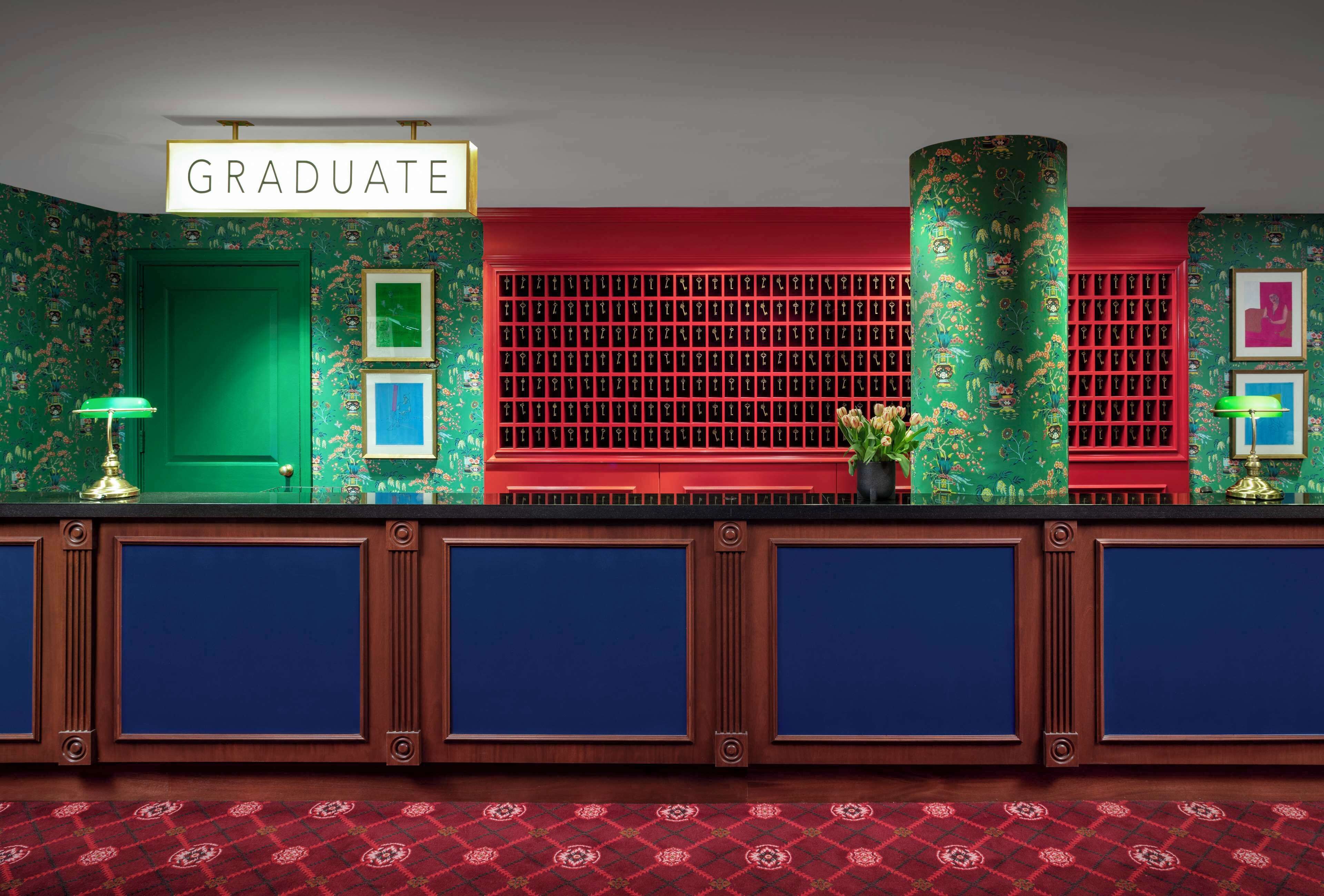 A reception area with a 'GRADUATE' sign, a green door, a red wall with a grid pattern, and a patterned carpet.