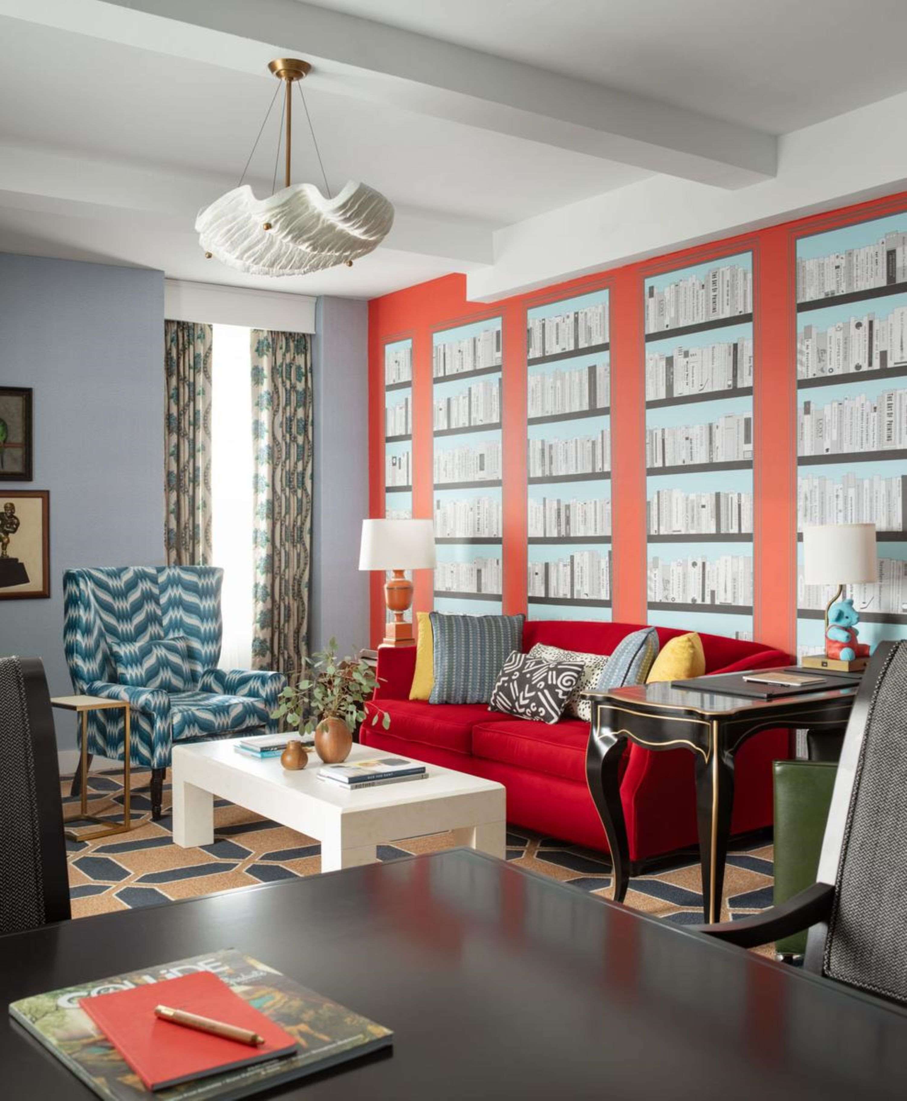 Un salon moderne avec un canapé rouge, un fauteuil bleu, une table basse et une bibliothèque remplie de livres.
