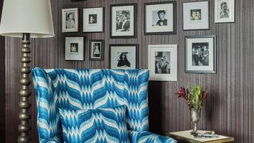 A room with a patterned armchair, a floor lamp, and a wall adorned with framed photographs.