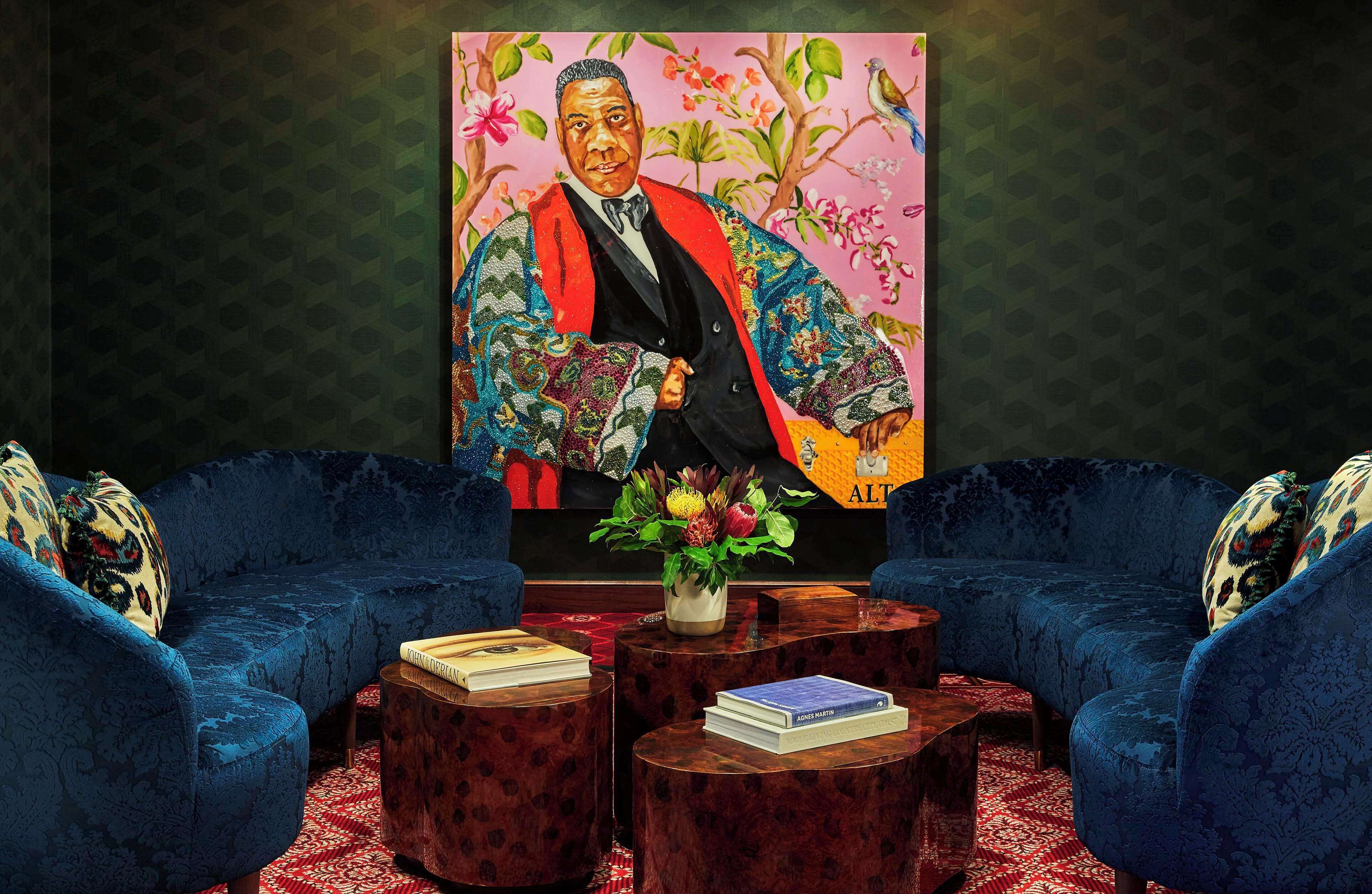 Um quarto com um grande retrato, dois sofás azuis, uma mesa de centro de madeira e um tapete vermelho estampado.