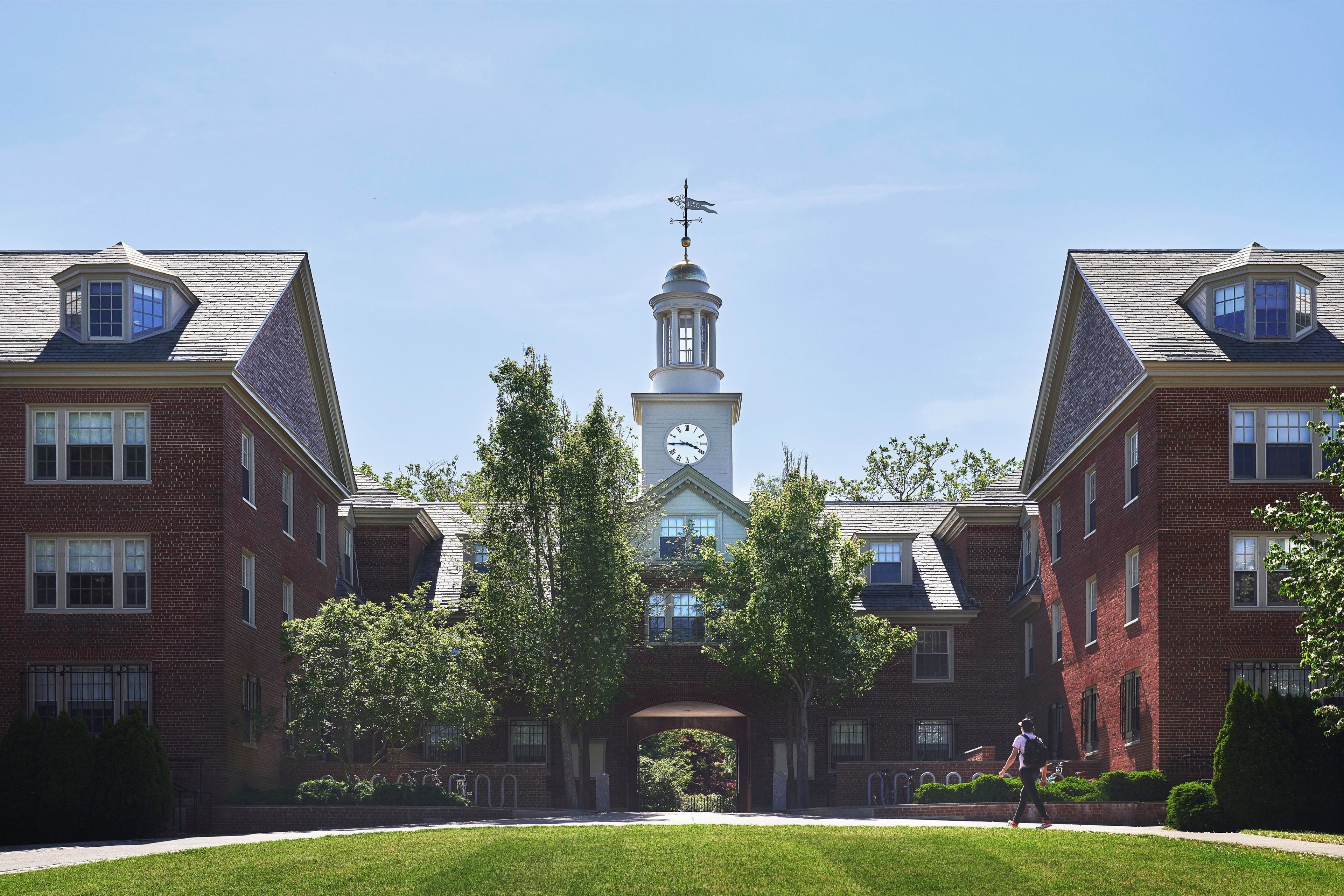 A large brick building with a central tower featuring a clock and a weather vane.